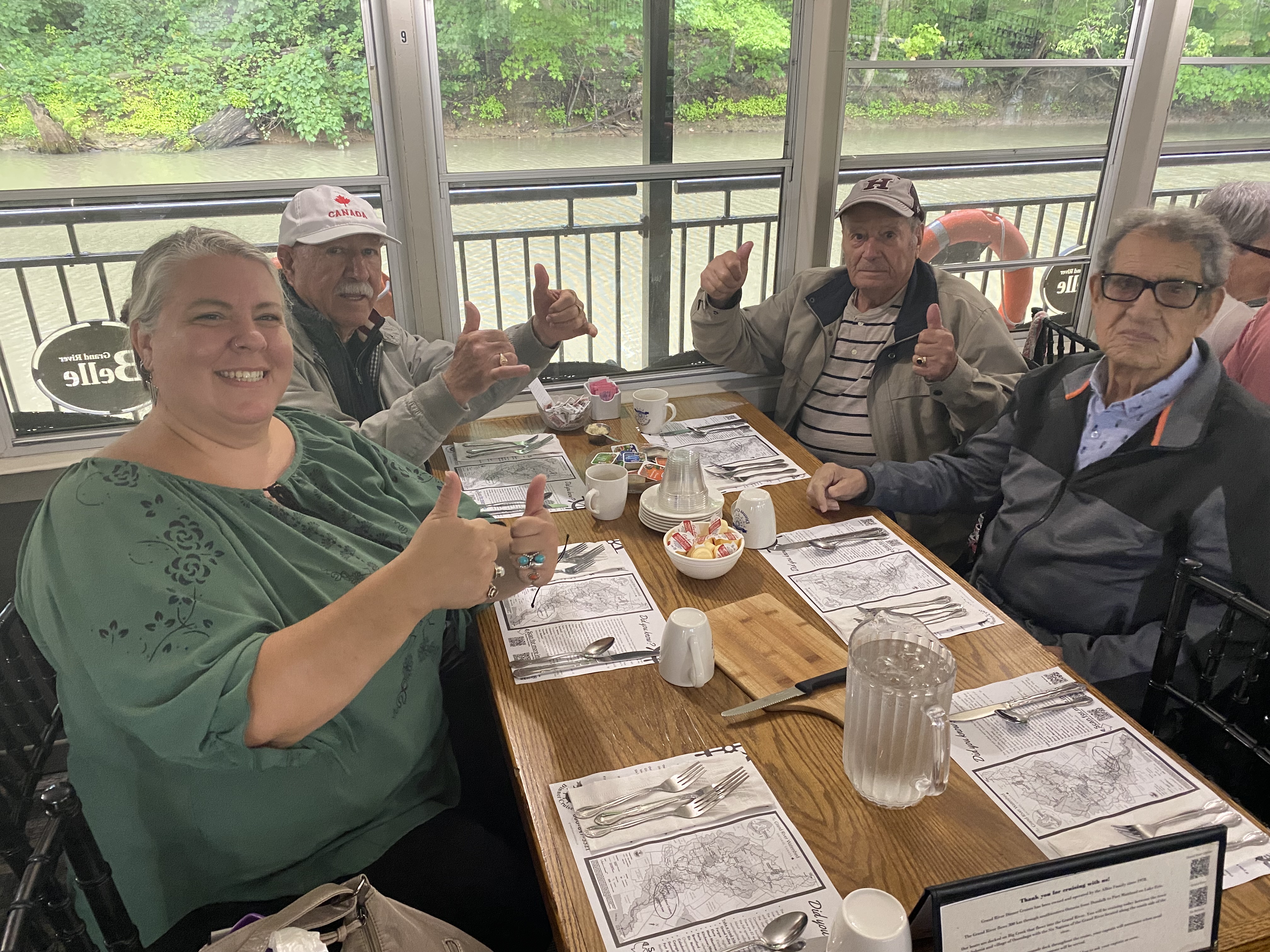 Group of adults sitting together at a restaurant table during an outing, giving thumbs up and enjoying a meal.