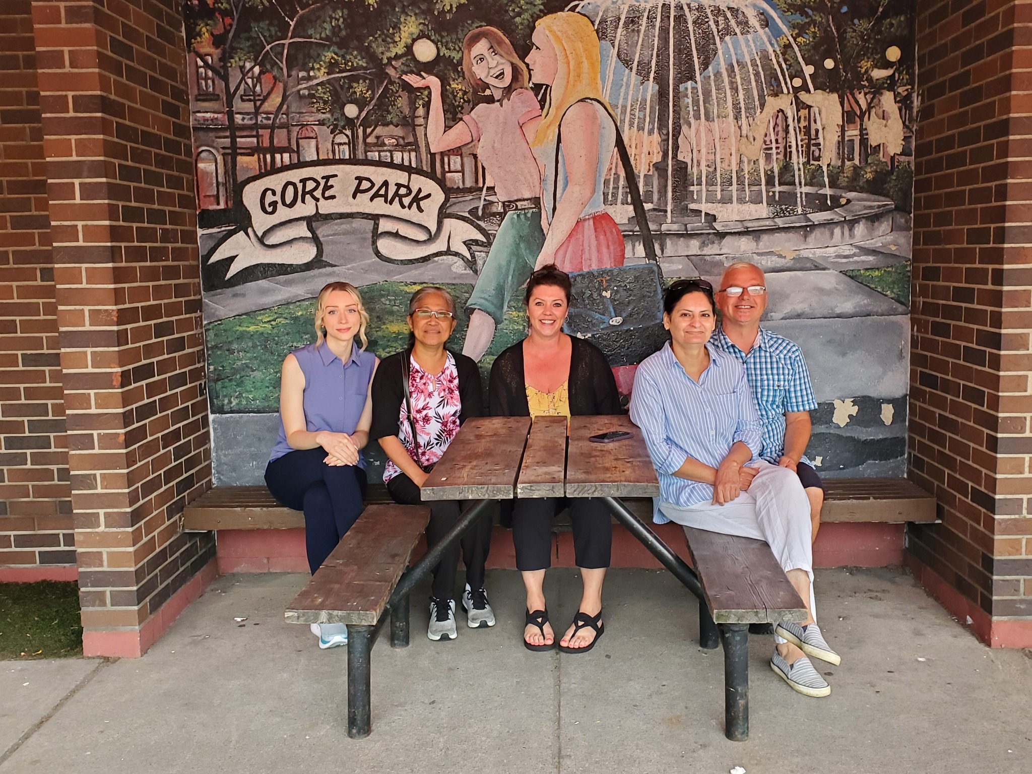 Group of team members sitting together on a bench in front of a Gore Park mural.