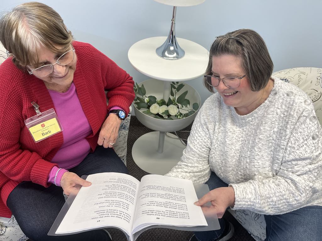 Two women sitting together indoors, reviewing a book during a worship services activity.